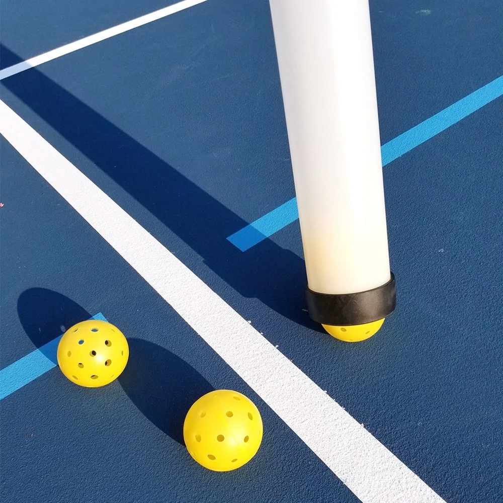 Een transparante Tourna Pickleball Ball Tube gevuld met gele pickleballen op een pickleballbaan.